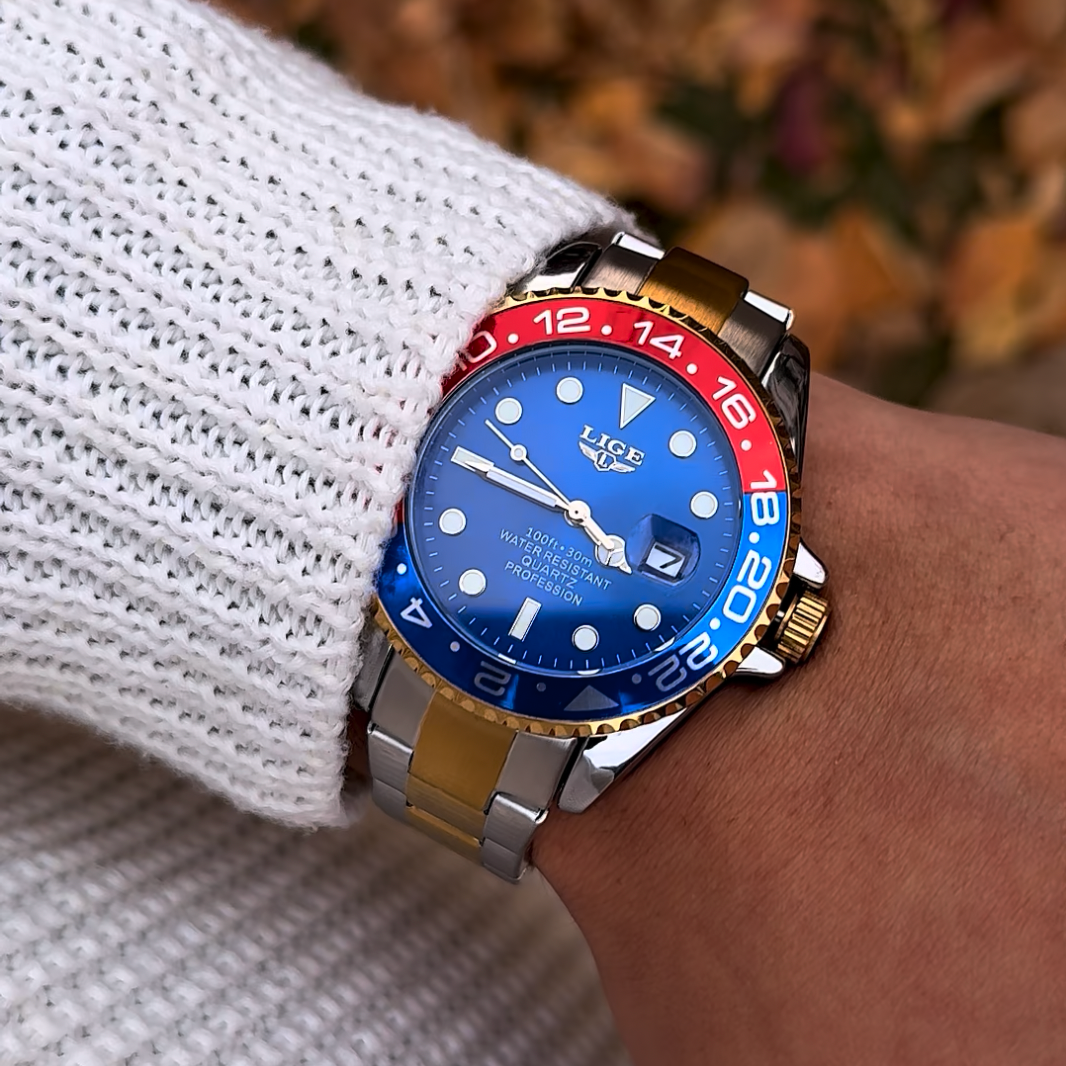 Close-up of a wrist wearing a watch with a blue face and red accents, against a blurred natural background.