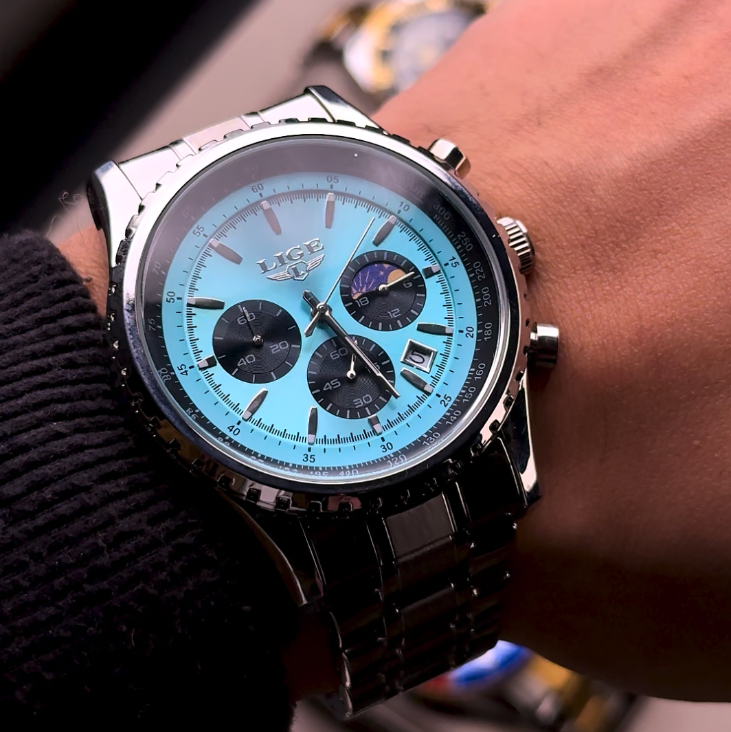 Wrist wearing a watch with a blue face and black strap, blurred background