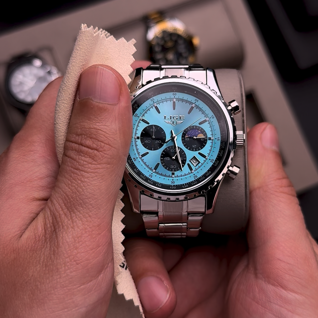 Una mano sostiene un reloj con esfera azul y caja marrón, limpiándolo con un paño.